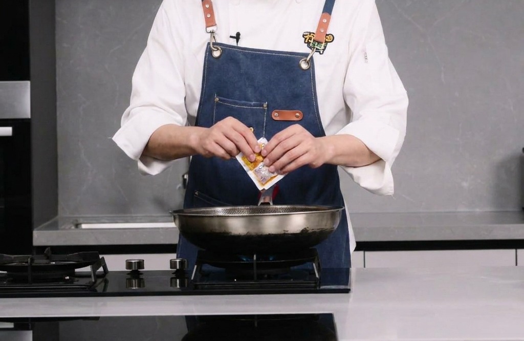 Una persona abriendo un pequeño paquete de base picante para hot pot sobre un wok.