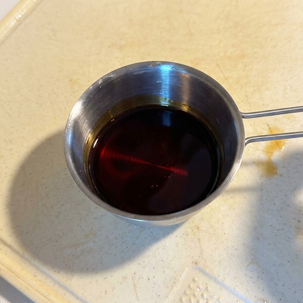 Una mezcla de salsa oscura y brillante en un pequeño recipiente medidor de acero inoxidable.