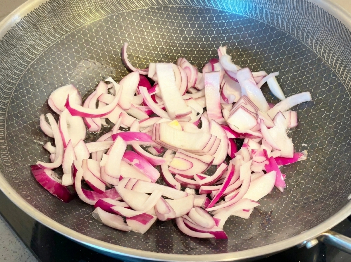 Láminas de cebolla roja salteándose en una sartén de metal.