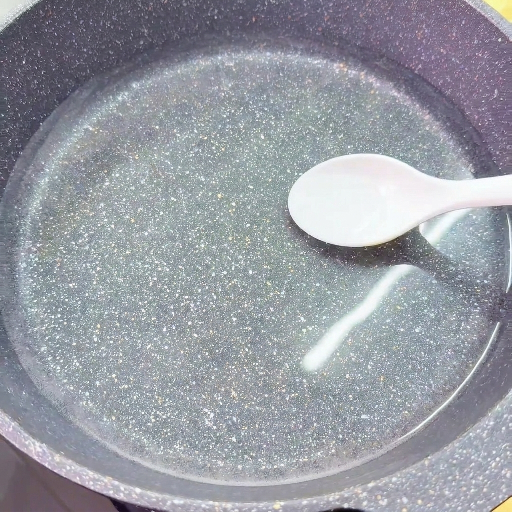 Una cuchara blanca añade una porción de sal en un wok lleno de agua clara y fría.