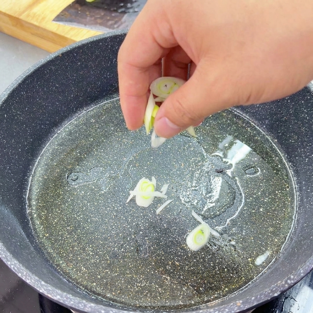 Rodajas de cebolleta verde y blanca se saltean en una capa de aceite en una sartén de granito oscuro.