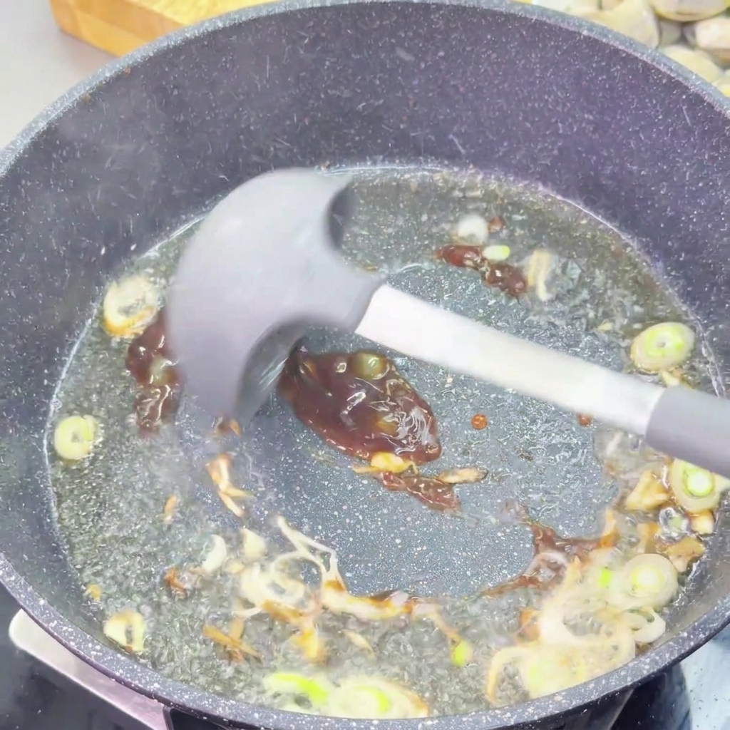 Una salsa de ostión oscura y espesa se incorpora a las cebolletas salteadas usando una espátula de silicona gris.