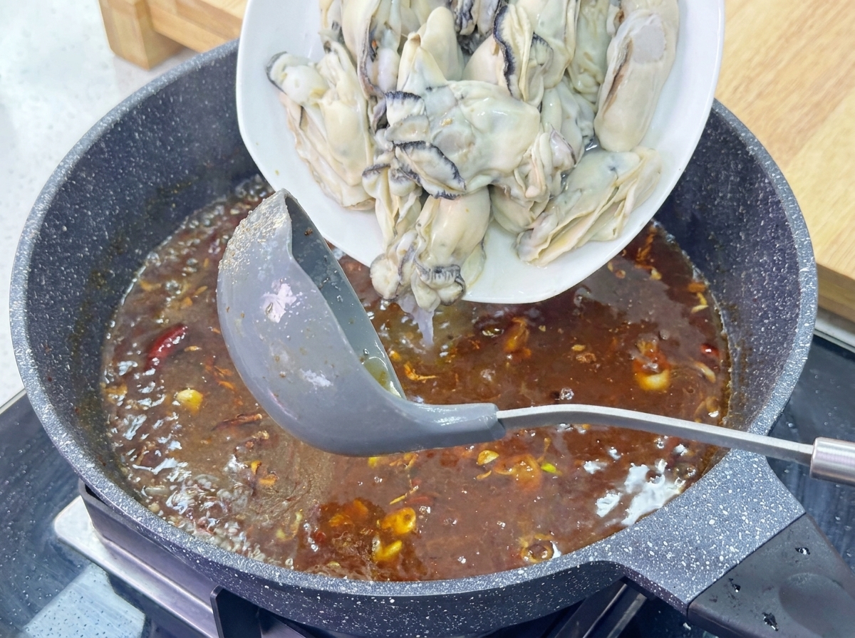 Un plato de ostras grandes y blanqueadas se desliza hacia una salsa marrón burbujeante en una sartén de granito.