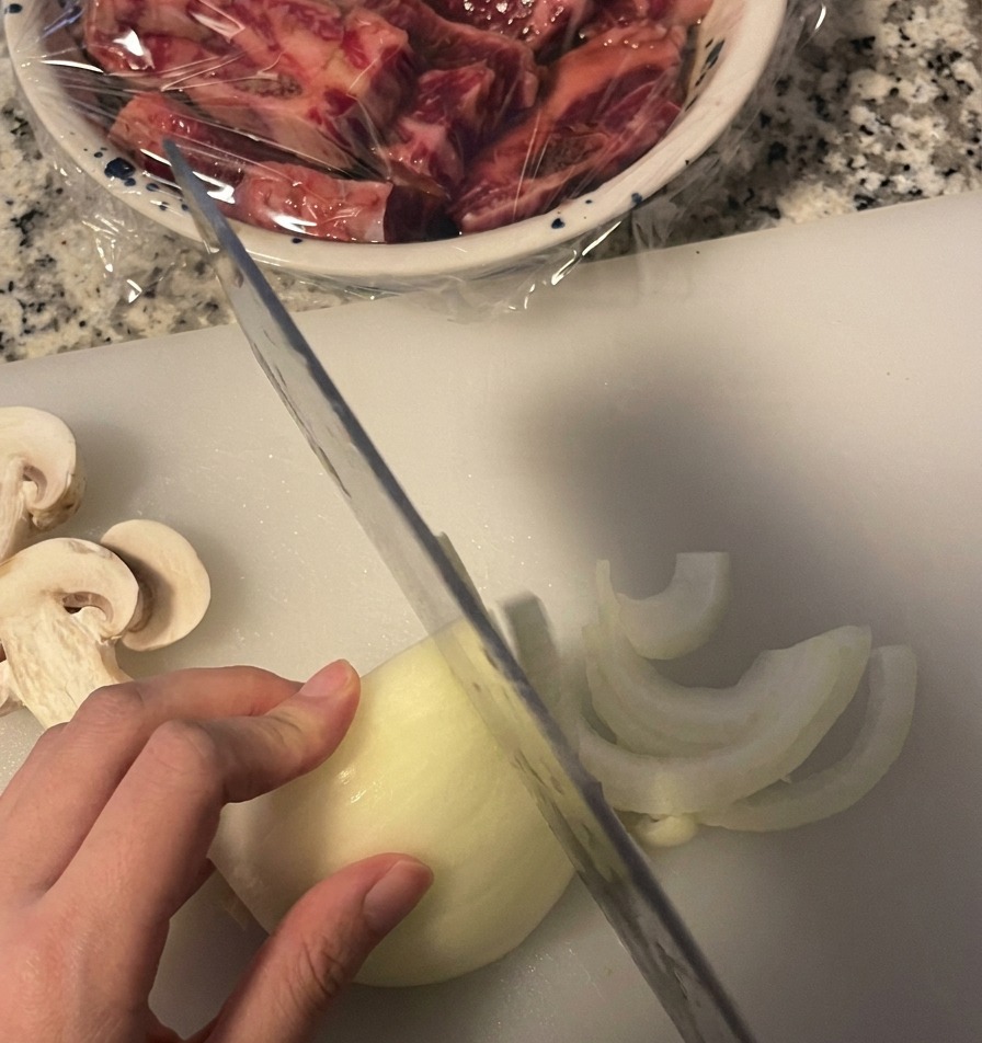 Una persona cortando una cebolla blanca en medias lunas finas sobre una tabla de cortar con un cuchillo de cocina.