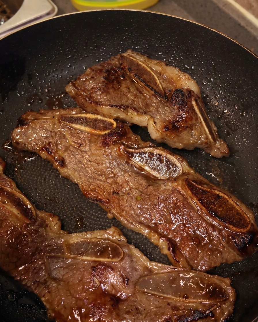 Tijeras de cocina cortando tiras de costilla de ternera doradas dentro de la sartén.