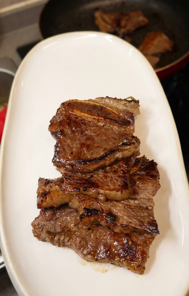 Pila de costillas LA jugosas y oscuras en un plato ovalado de cerámica blanca.