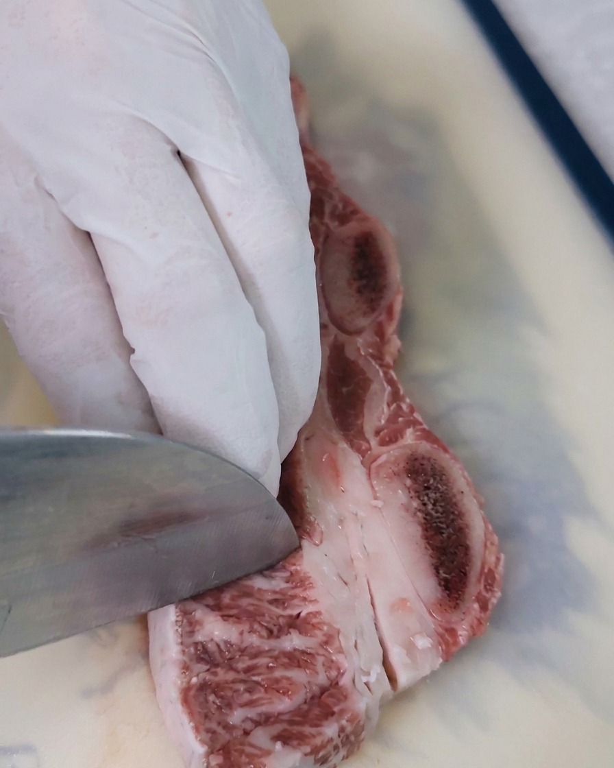 Primer plano de un cuchillo haciendo cortes diagonales en la carne roja de una costilla de res cruda para crear una textura ideal para el marinado.