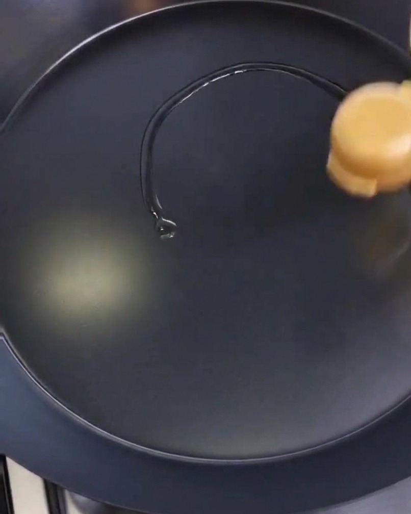 Una persona esparciendo una fina capa de aceite sobre la superficie de una sartén negra con un papel de cocina.