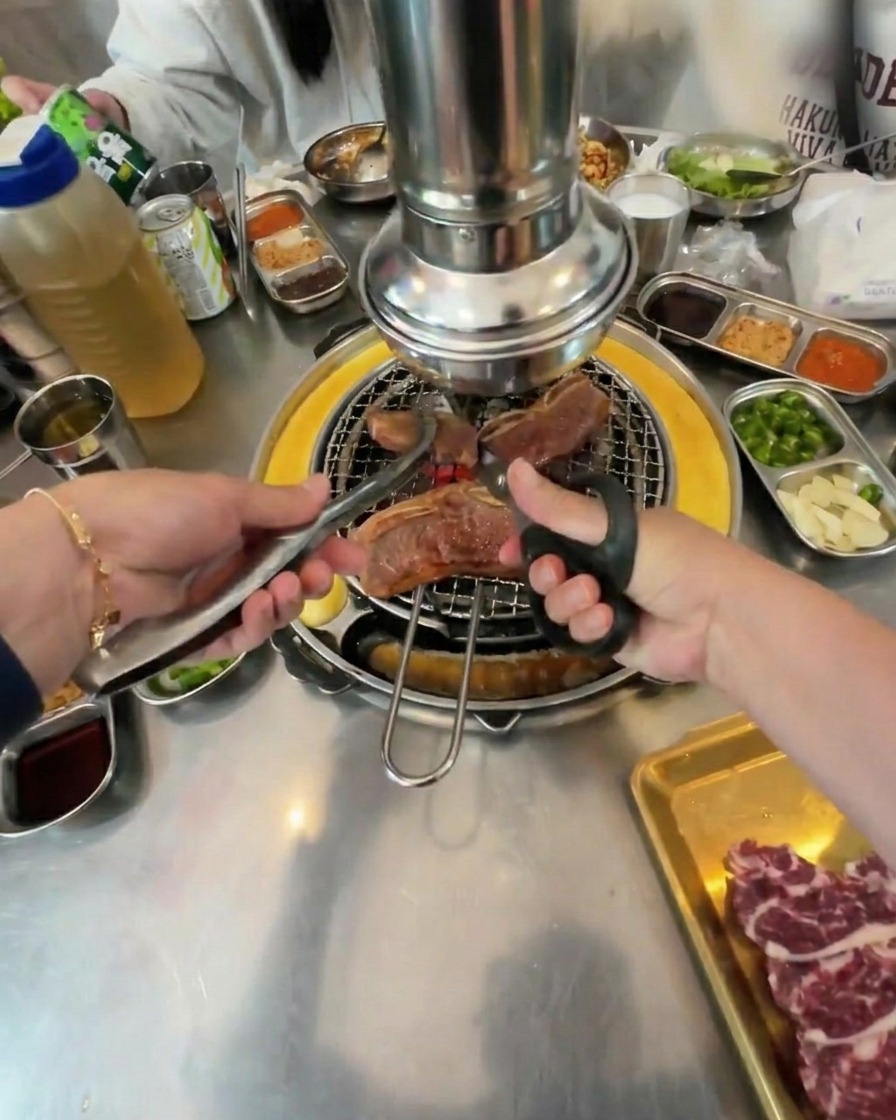 Corte de piezas grandes de ternera parcialmente cocinadas con tijeras de cocina y pinzas sobre una parrilla circular.