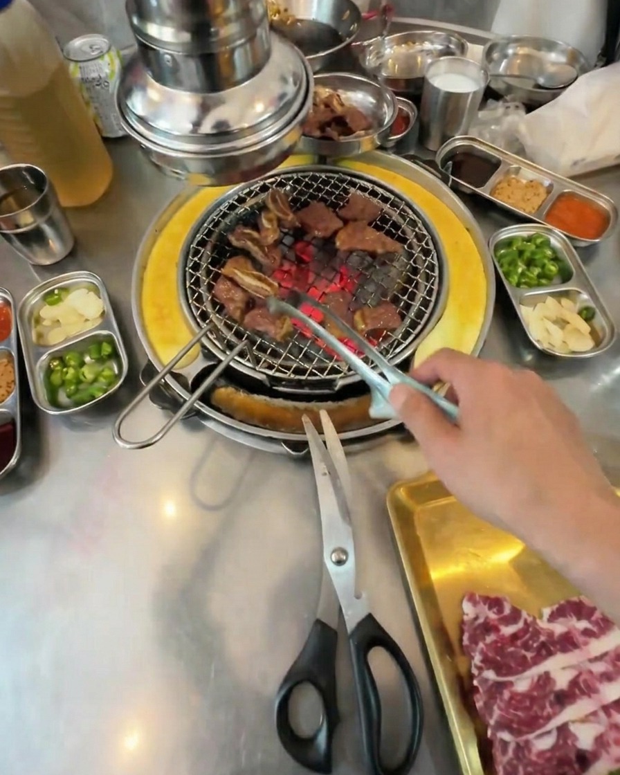 Pequeños cubos de ternera totalmente asados siendo removidos con pinzas sobre la rejilla de la parrilla.