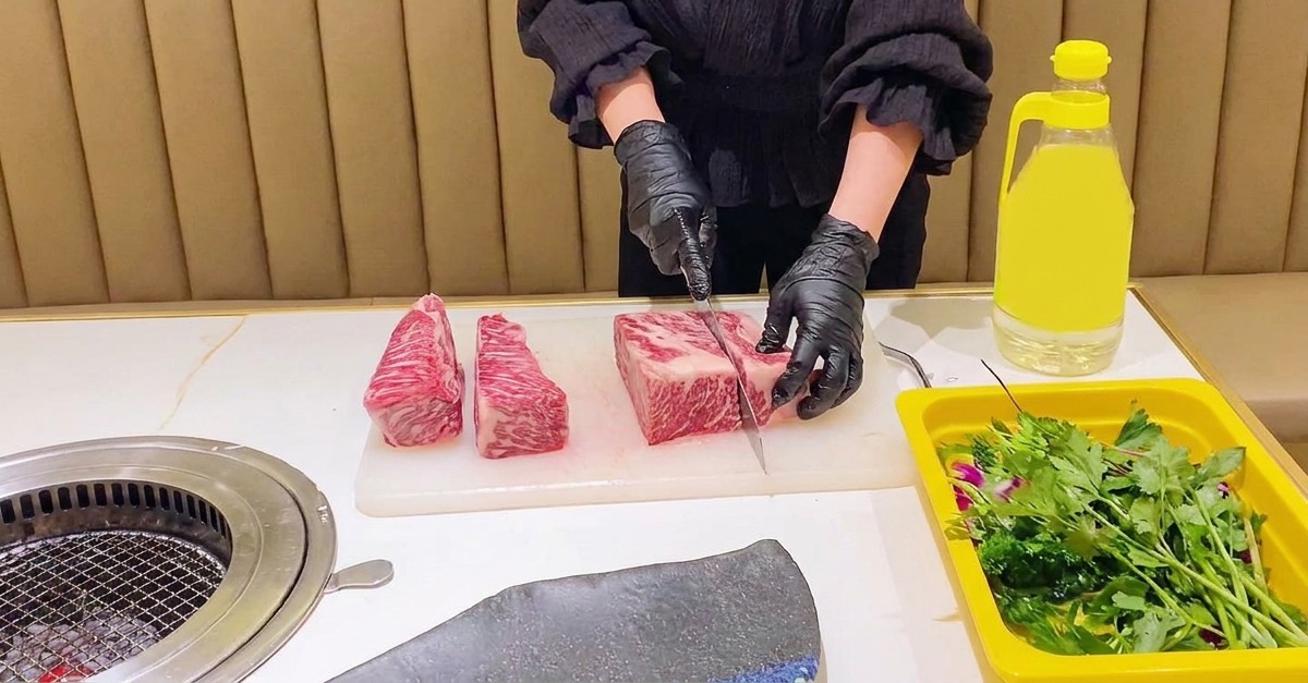 Persona con guantes negros usando un cuchillo de chef para dividir una costilla de ternera veteada en secciones rectangulares uniformes.