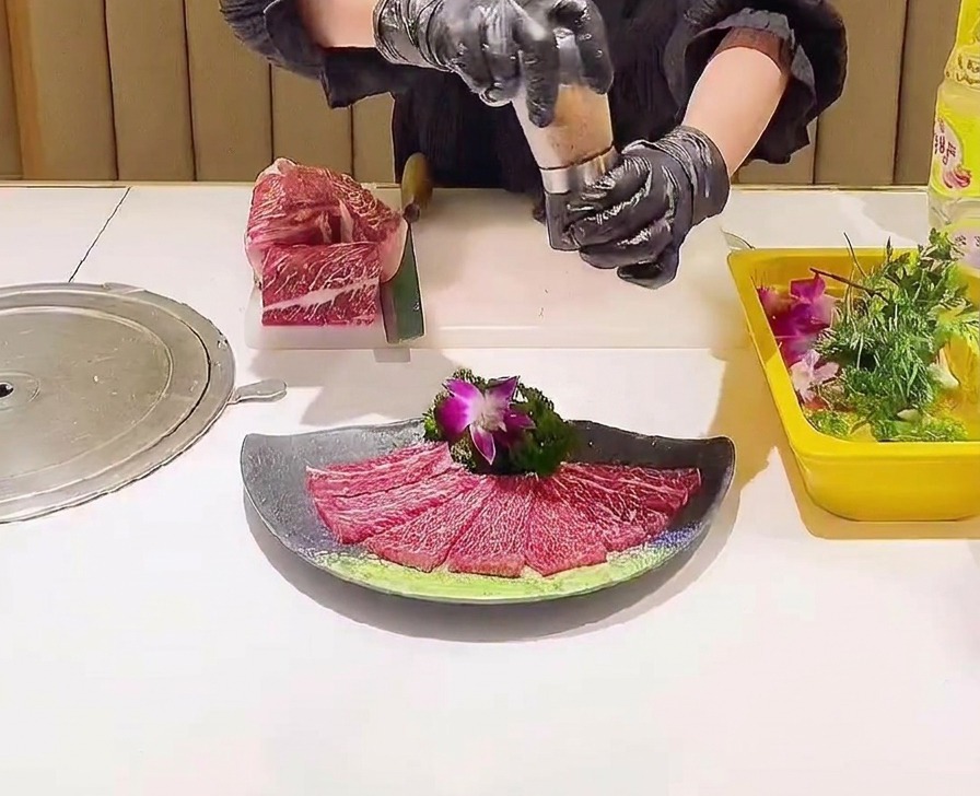 Un molinillo distribuyendo cristales de sal rosa sobre una disposición decorativa de láminas de ternera cruda veteada.