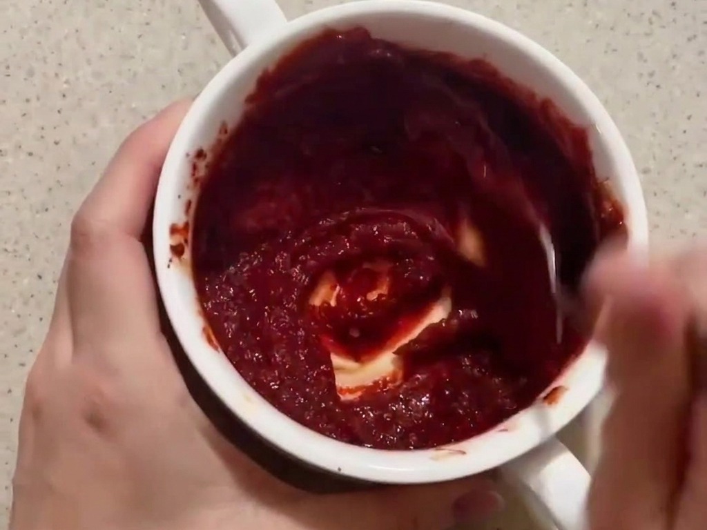Una persona mezclando una salsa roja espesa a base de gochujang en un pequeño bol blanco.