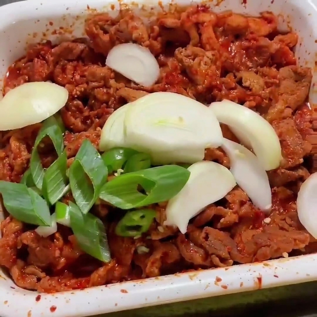 Cebollas blancas y cebolletas cortadas sobre tiras de cerdo picante chisporroteando en una sartén.