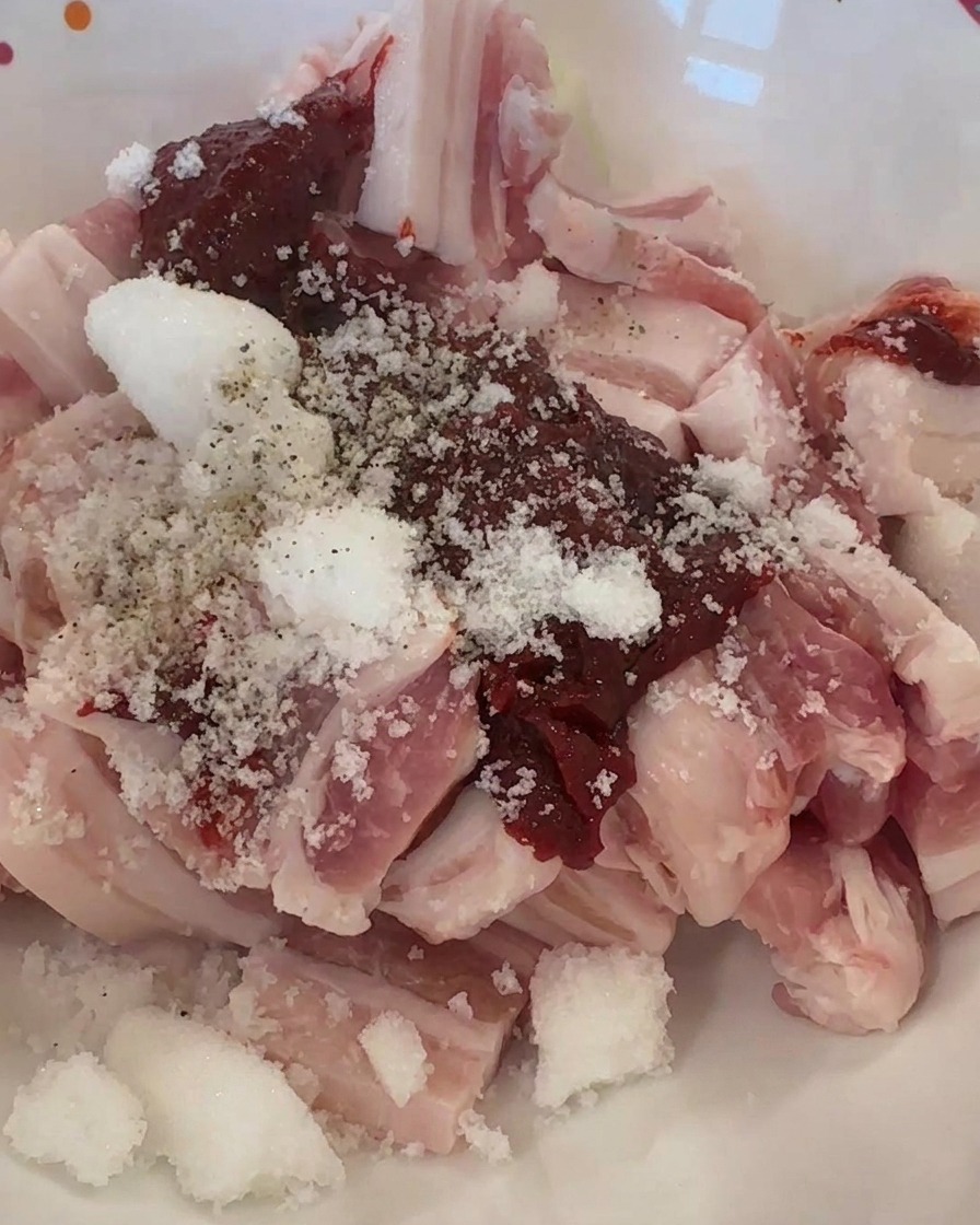 Tiras de cerdo crudo en un bol cubiertas con pasta de chile rojo, azúcar blanco y pimienta negra.