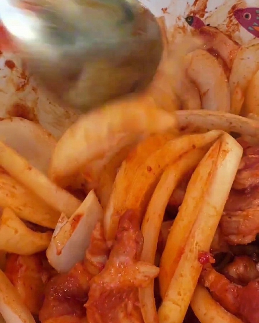 Rodajas grandes de cebolla blanca siendo mezcladas con la carne de cerdo marinada en rojo intenso.