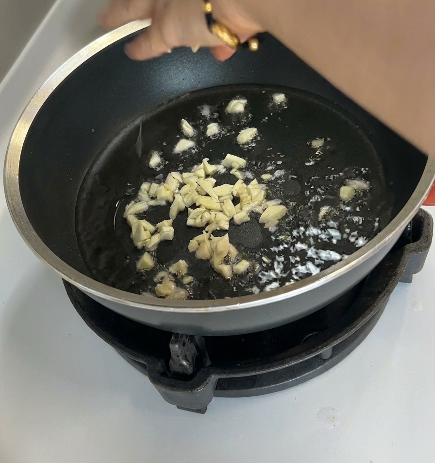 Ajo picado dorándose ligeramente en aceite caliente al fondo de una sartén antiadherente.