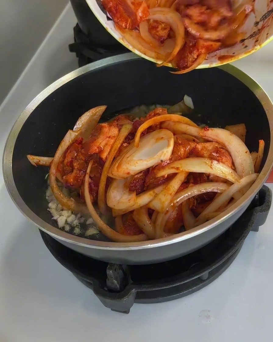 El cerdo picante y las cebollas salteándose en la sartén con vapor y la salsa burbujeando intensamente.