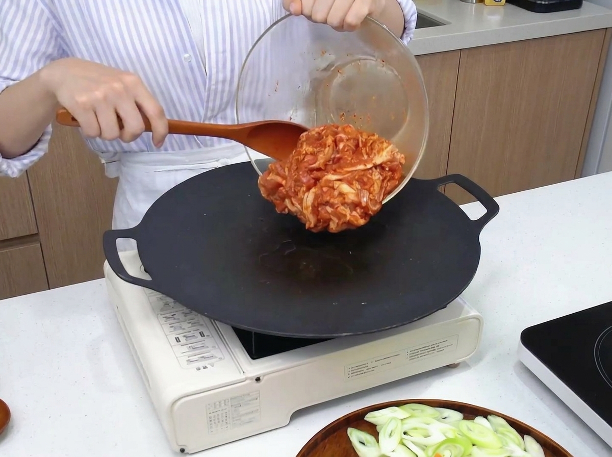Panceta de cerdo marinada pasando de un bol de cristal a una plancha circular caliente usando una espátula de madera.