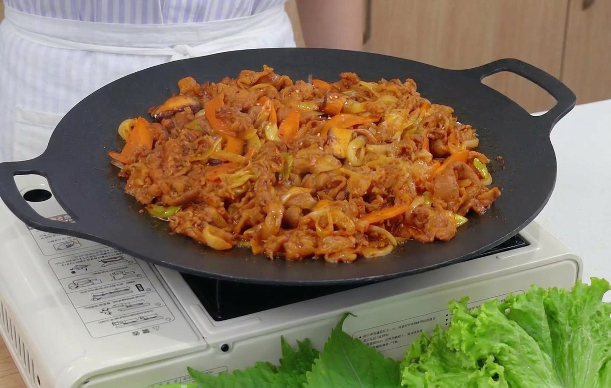 Primer plano de semillas de sésamo tostadas siendo espolvoreadas sobre una sartén humeante de cerdo picante y verduras.