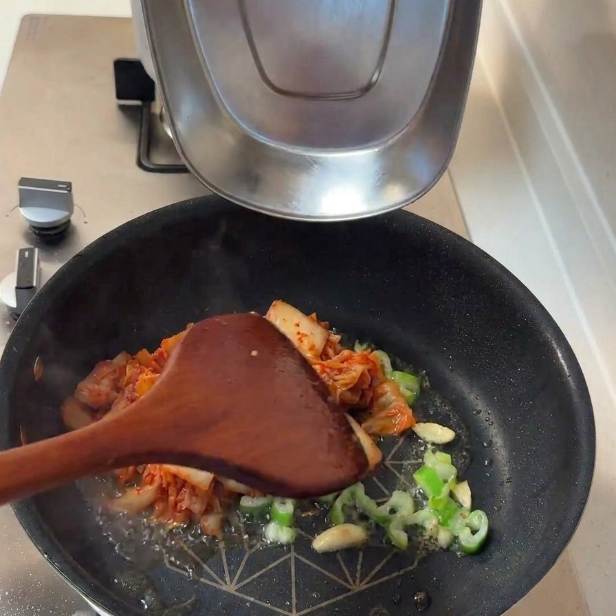Kimchi fermentado y rodajas gruesas de cebolla blanca añadiéndose a la sartén con el sofrito aromático.