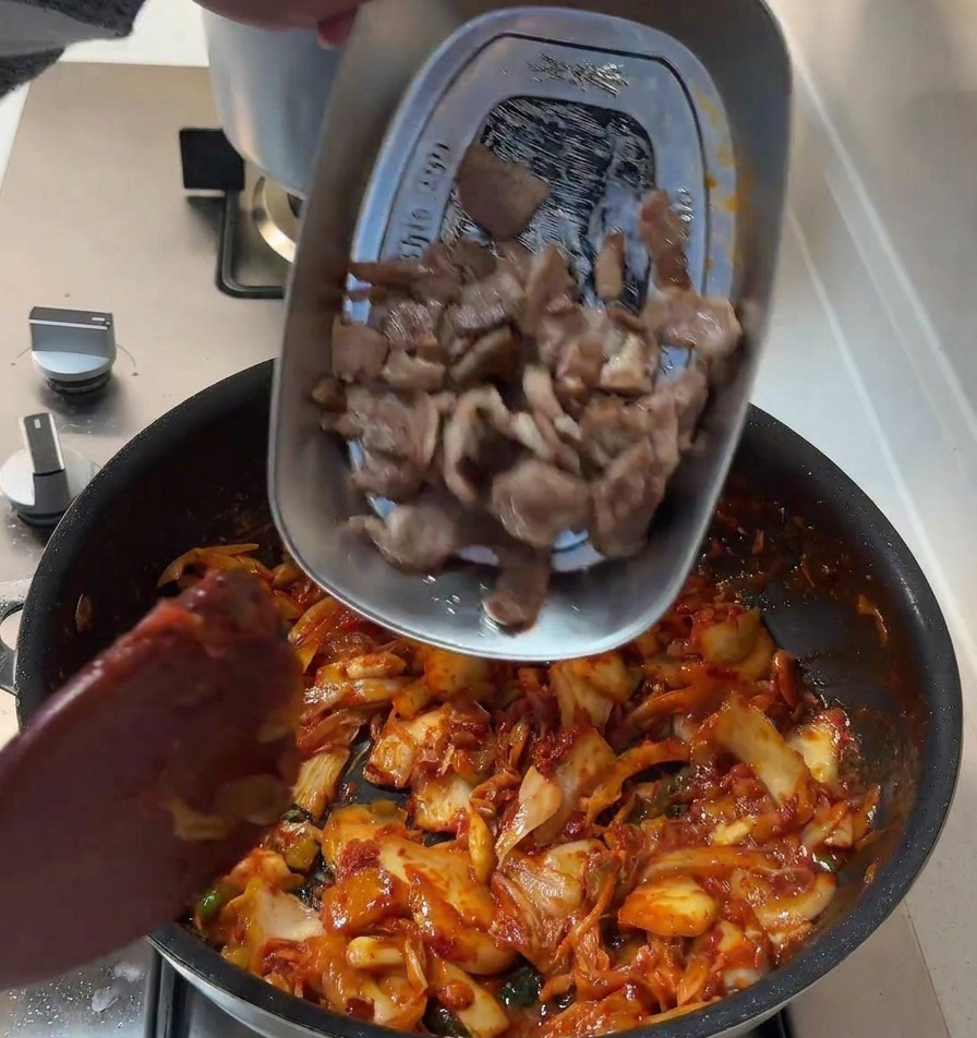 Láminas de cerdo selladas volviendo a la sartén que contiene la mezcla roja de kimchi y cebolla.