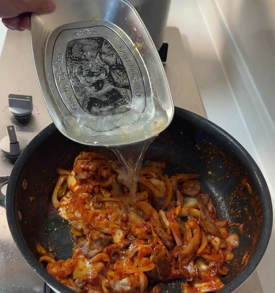 Agua vertiéndose en la sartén con el cerdo picante y el kimchi para terminar de ligar la salsa.