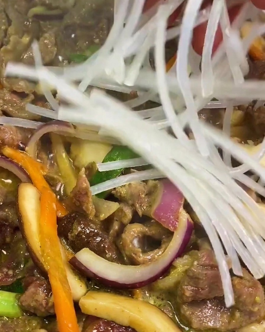 Una mano soltando fideos de batata transparentes e hidratados en una sartén con ternera y verduras.