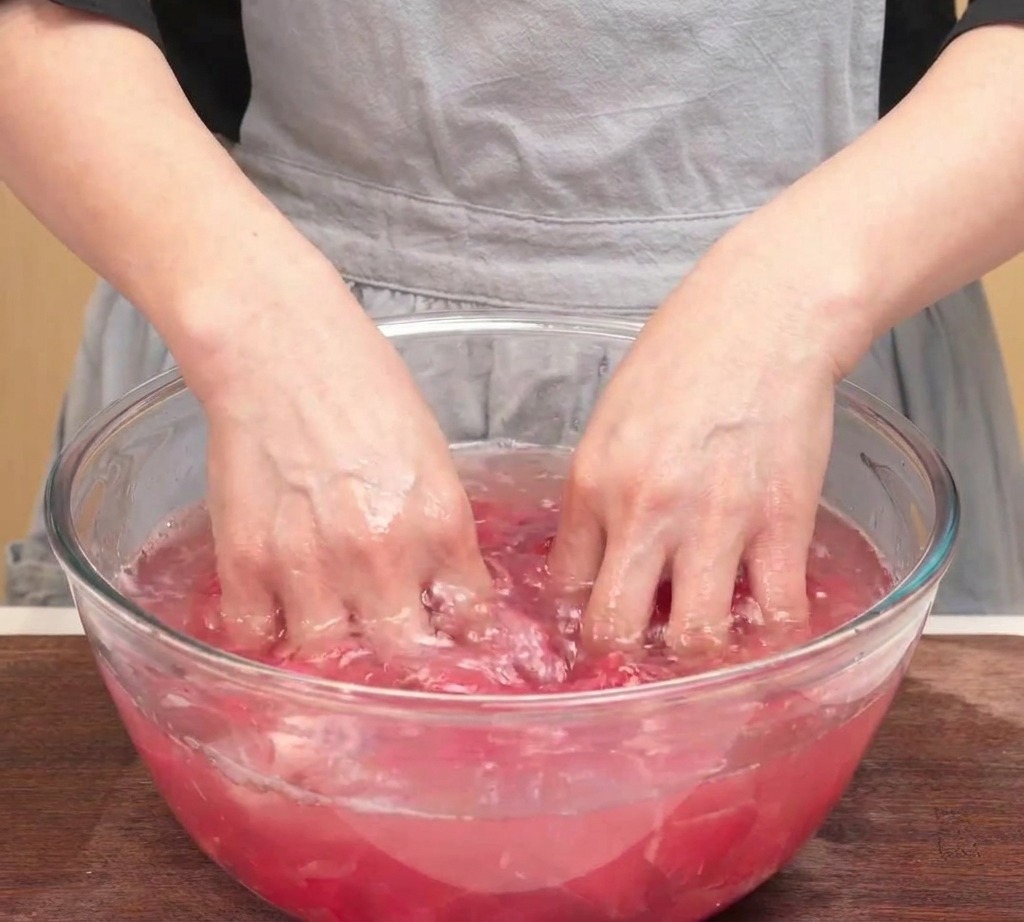 Manos presionando láminas de ternera cruda sobre un bol de cristal para eliminar el exceso de agua.