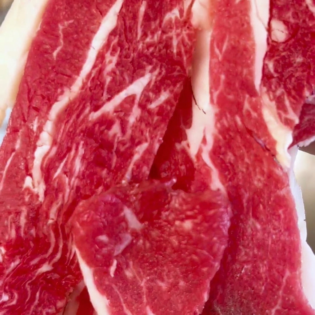 Primer plano de láminas de ternera fresca y veteada en un bol de acero inoxidable.