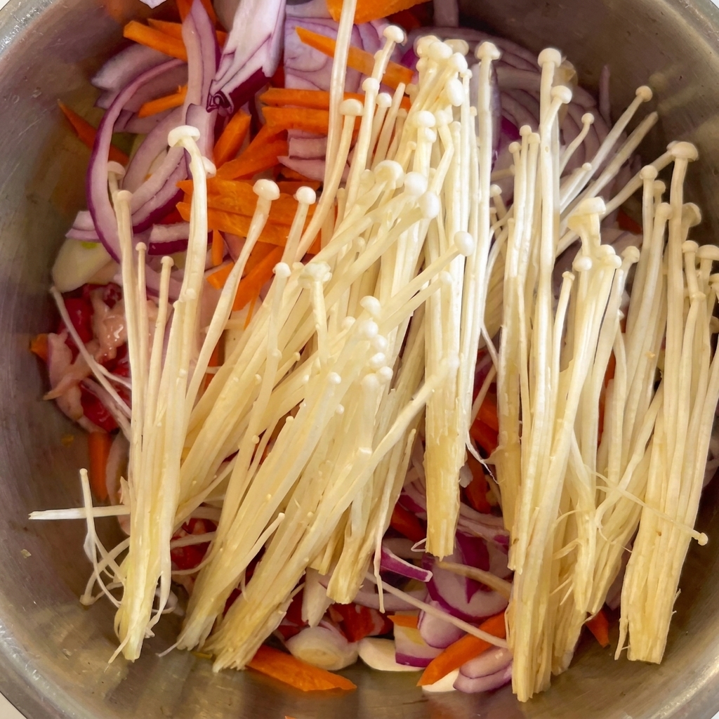 Setas enoki frescas y ajo picado colocados sobre la carne, la cebolla y la zanahoria.