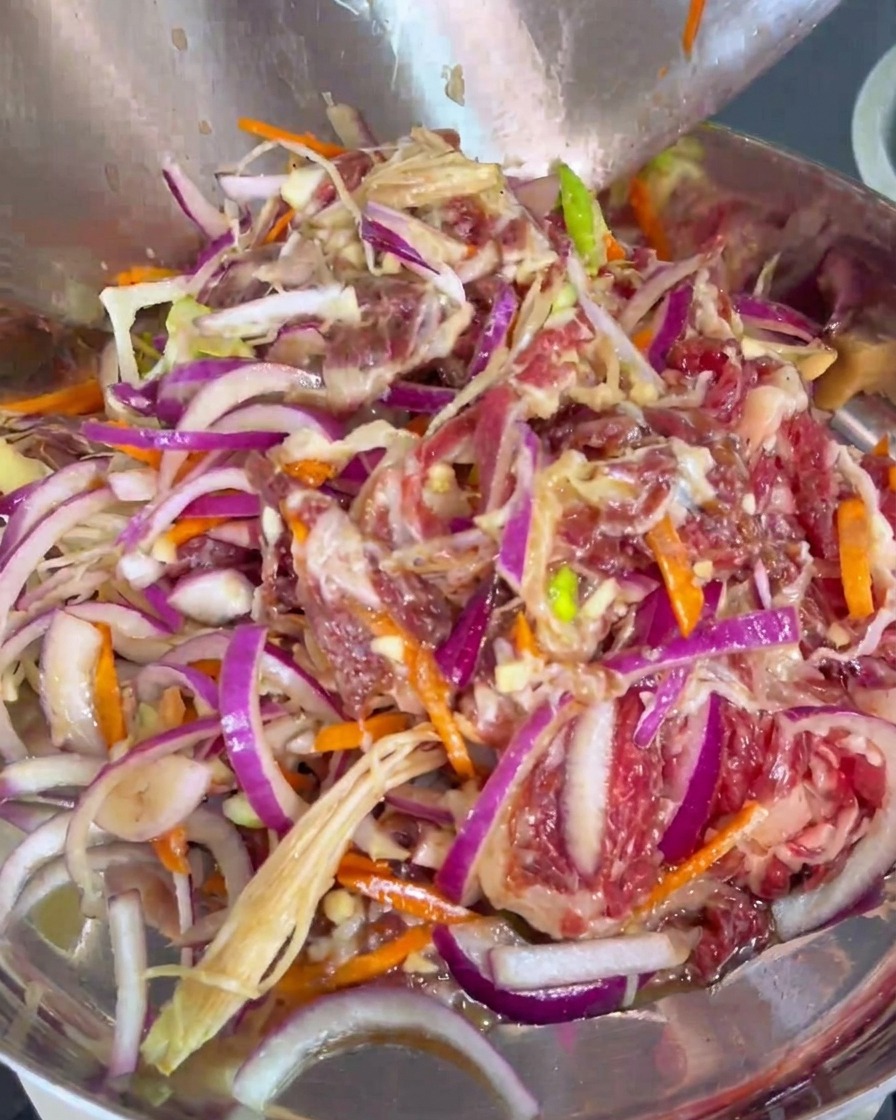 Carne marinada mezclada con cebolla y zanahoria pasándose a una sartén de cocina.
