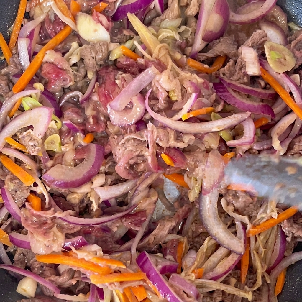 Tiras de carne marinada y vegetales variados cocinándose en una sartén caliente.