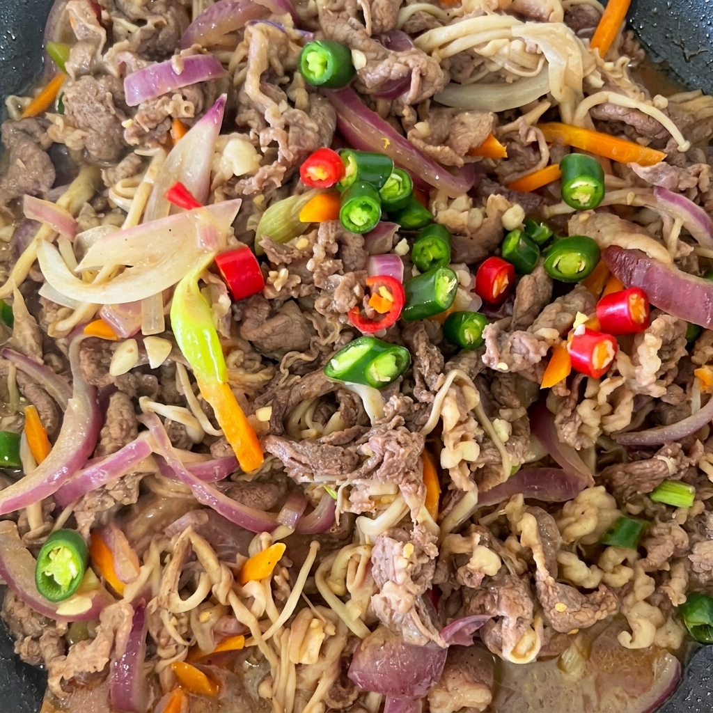 Chiles rojos y verdes en rodajas sobre el bulgogi de ternera ya cocinado en la sartén.