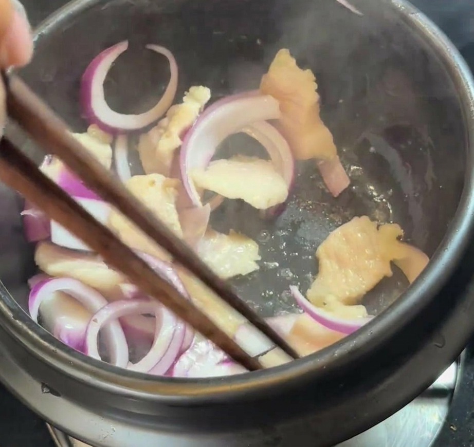 Cebolla morada en rodajas mezclándose con la panceta dorada dentro de la olla.