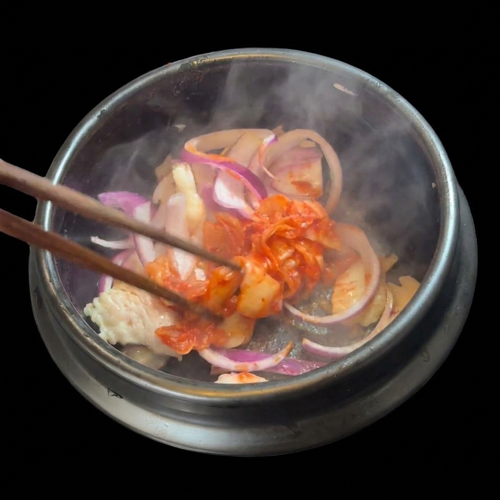 Kimchi rojo troceado añadiéndose a la mezcla de cerdo y cebolla en la cazuela.