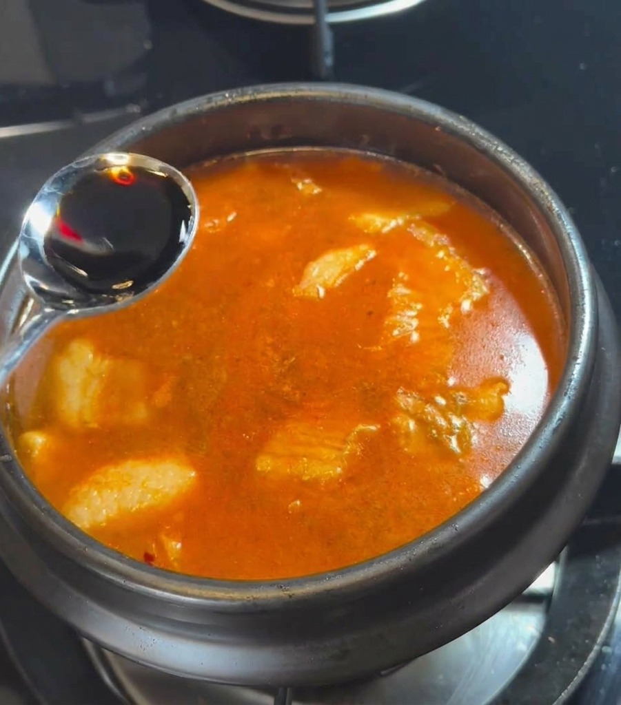 Una cuchara vertiendo salsa de soja oscura en el caldo rojo que burbujea.
