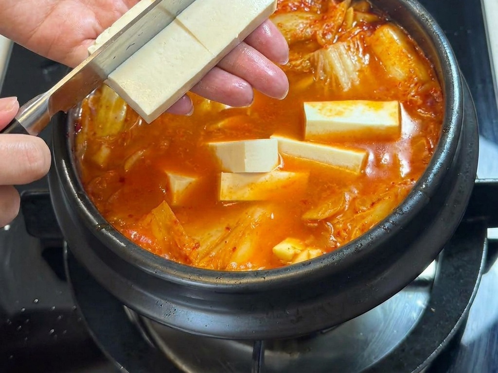 Una persona cortando un bloque de tofu blanco directamente sobre el estofado picante.