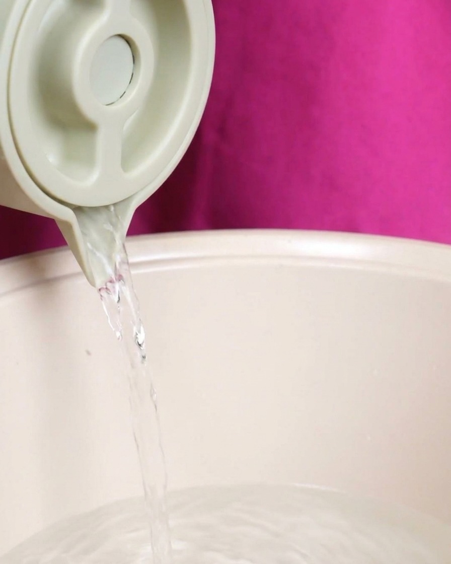 Un chorro constante de agua clara vertiéndose desde una jarra clara en una olla grande que contiene los ingredientes de la sopa.
