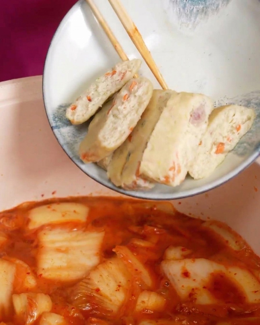 Láminas de pasteles de pescado cayendo en una sopa de kimchi roja y burbujeante.