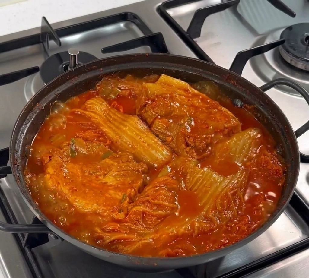 Una cuchara de metal colocando ajo picado sobre la superficie de la panceta cruda en una sartén.