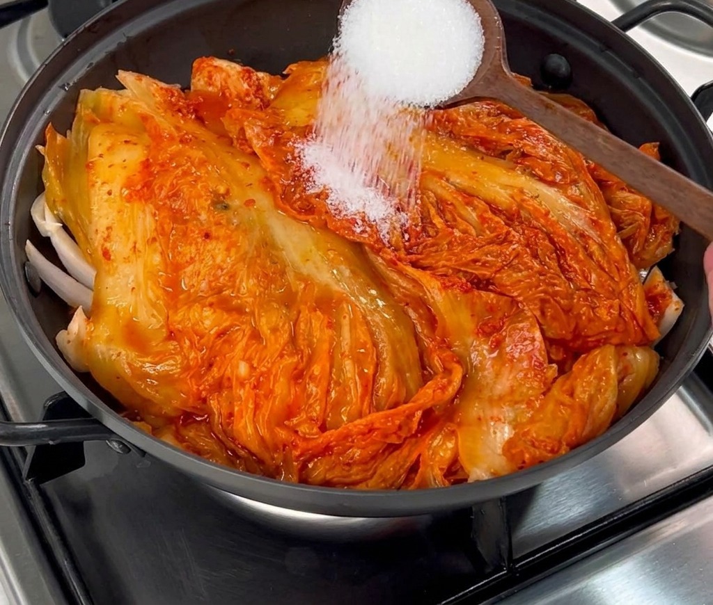 Azúcar blanca granulada espolvoreándose desde una cuchara de madera sobre el kimchi rojo.
