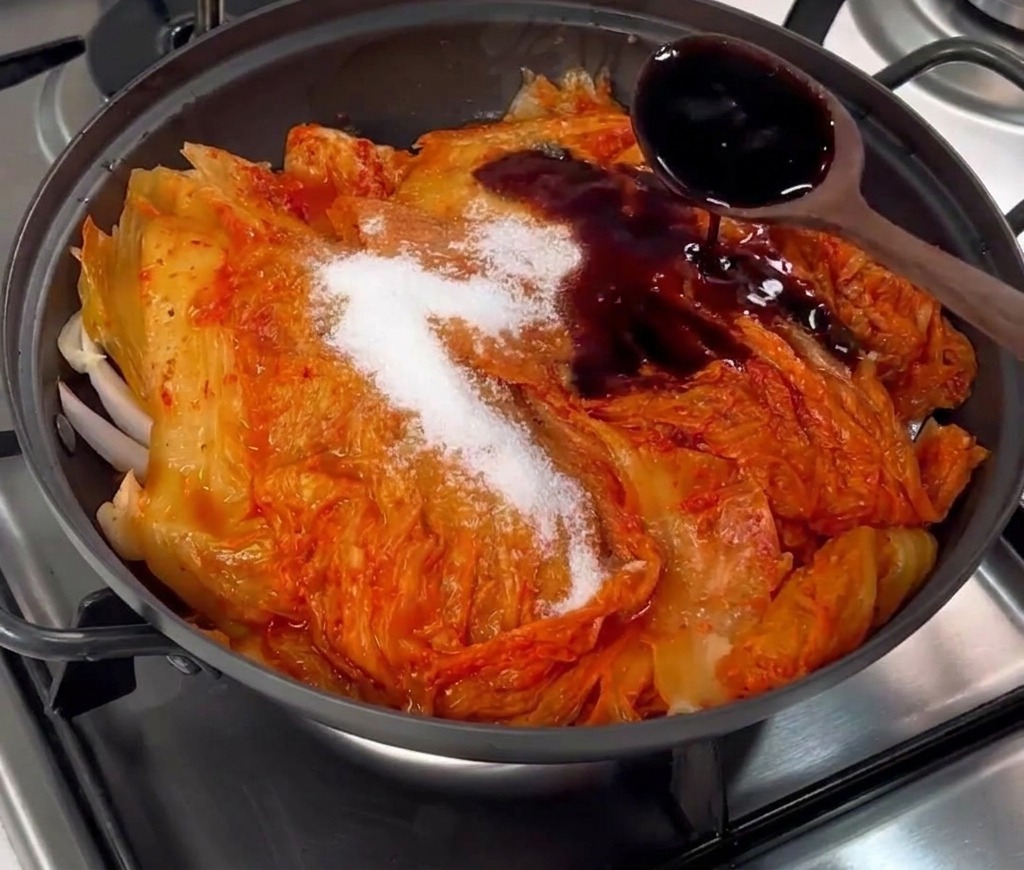 Salsa de soja oscura vertiéndose desde una cuchara sobre el kimchi y el azúcar.