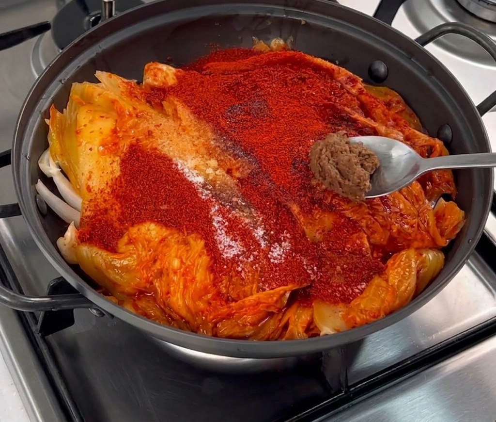Una pequeña porción de pasta de soja marrón sobre una cuchara de metal colocada sobre el chile y el kimchi.