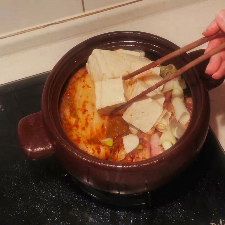 Rodajas de tofu blanco colocándose sobre los ingredientes del estofado en una olla de barro con palillos.