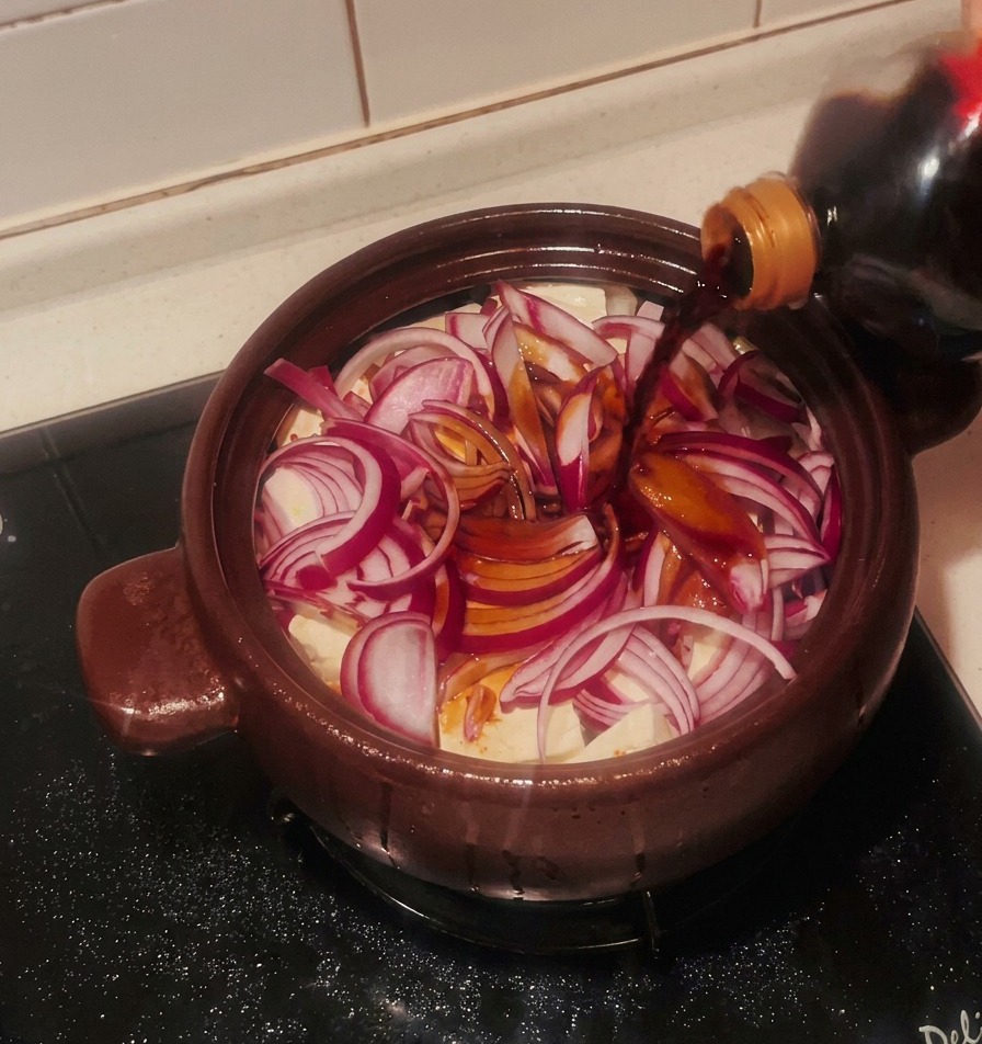 Salsa de soja oscura vertiéndose desde una botella sobre la cebolla roja y los bloques de tofu.