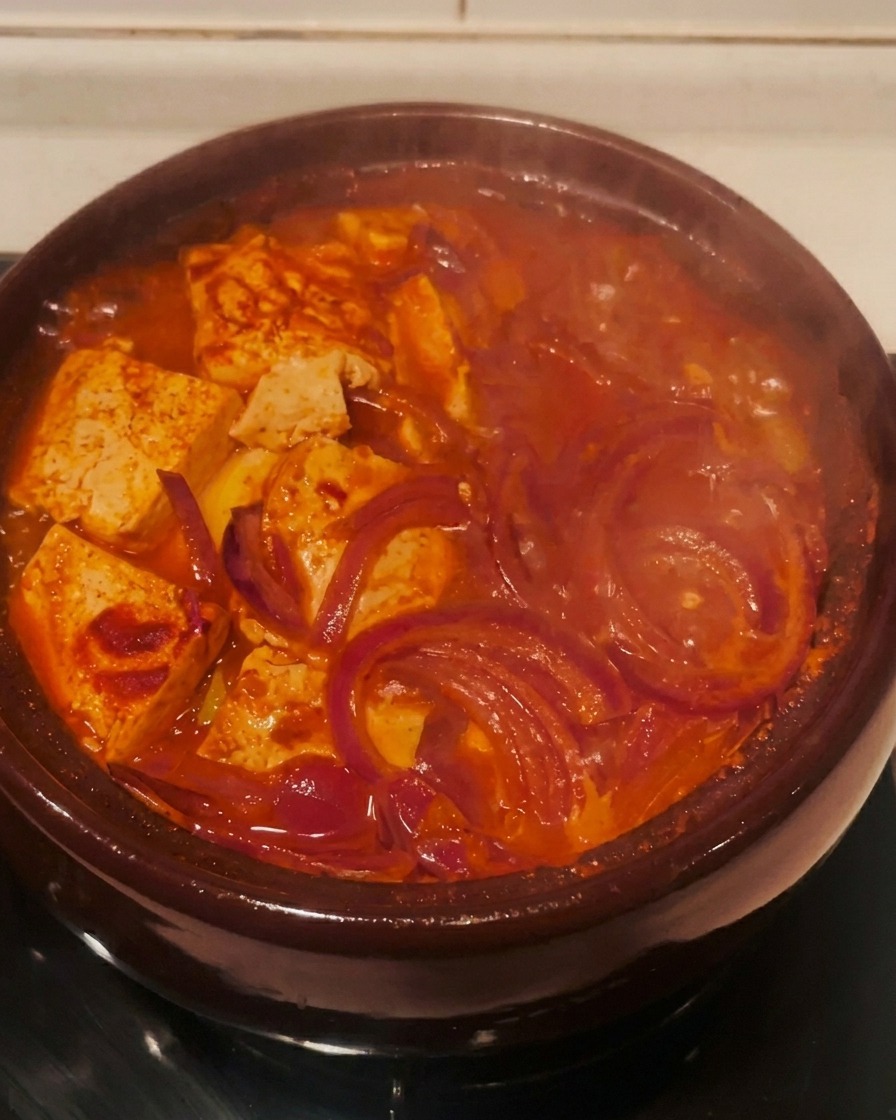 El estofado de kimchi rojo burbujeando activamente en una olla de barro sobre un quemador.
