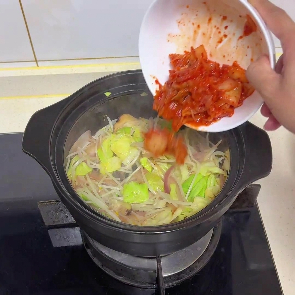Kimchi picado de color rojo vibrante vertiéndose desde un cuenco blanco a la olla con verduras salteadas.