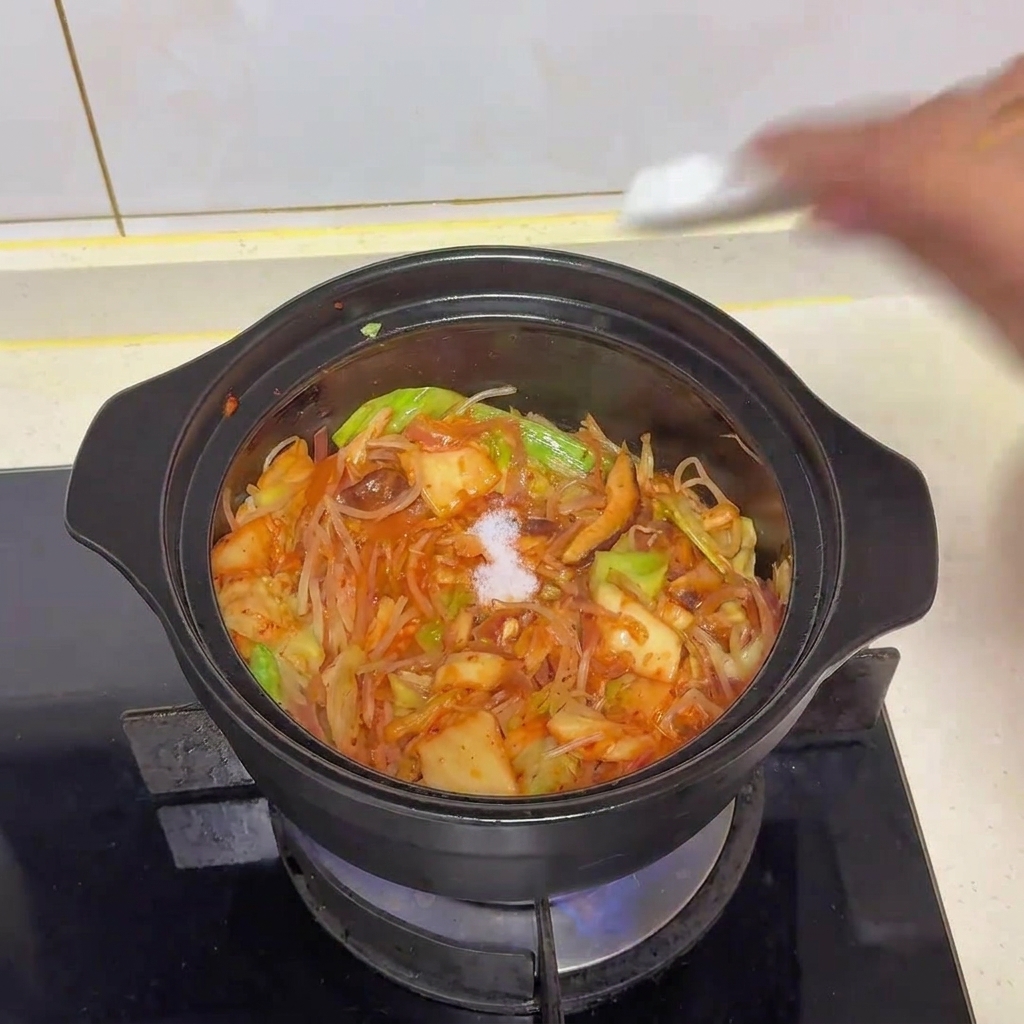 Una pizca de sal blanca añadiéndose a la olla de verduras y kimchi salteados.