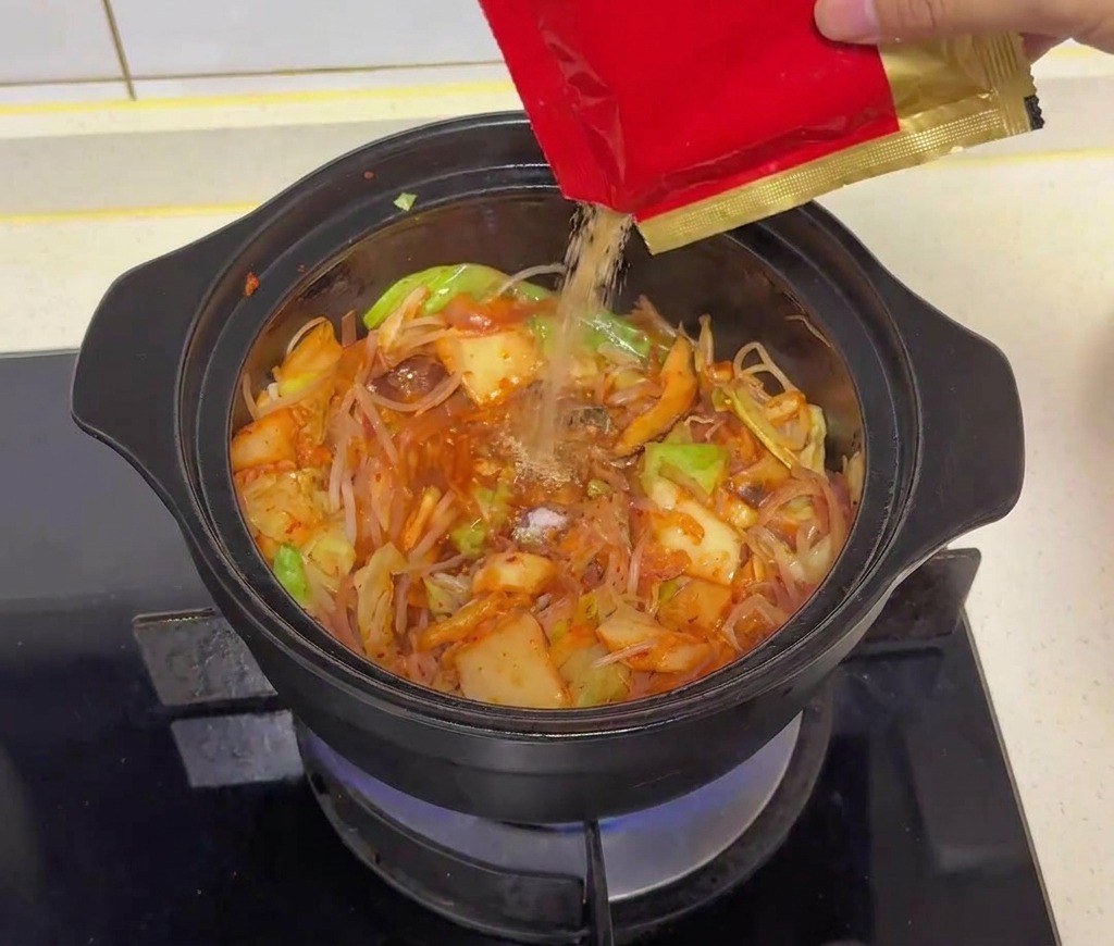 Sazonador de carne en polvo vertiéndose desde un paquete rojo y dorado a la mezcla de la olla.